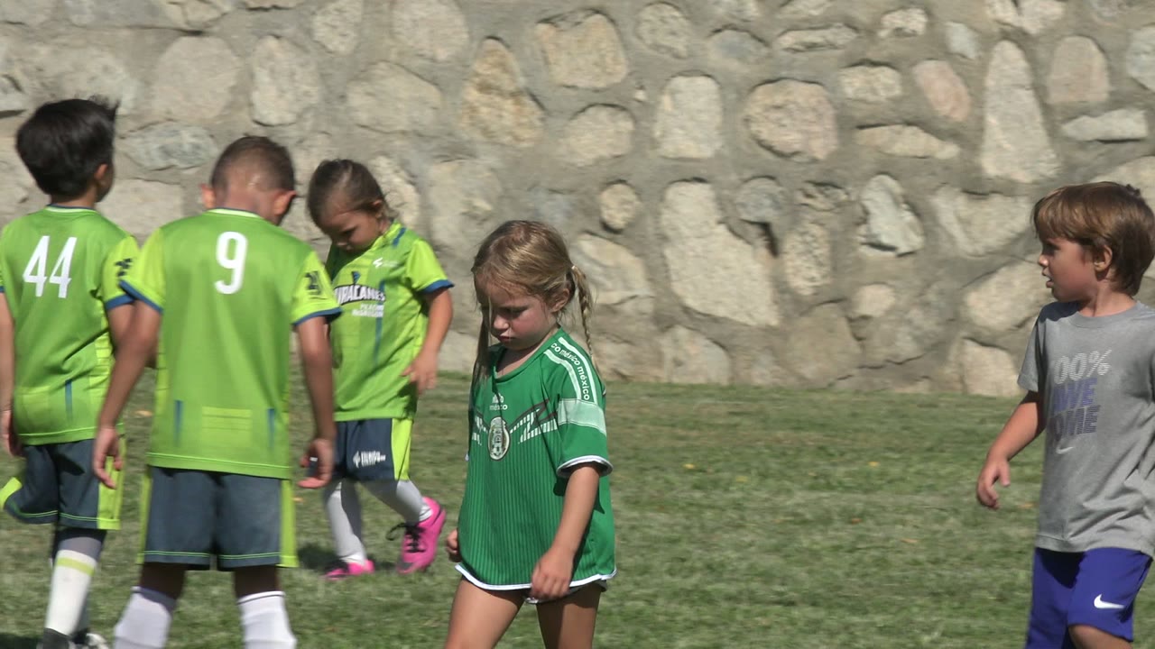Two children in bright green soccer jerseys face away while a girl in a green jersey and a boy in gray move through the frame in San Jose Del Cabo, Mexico.