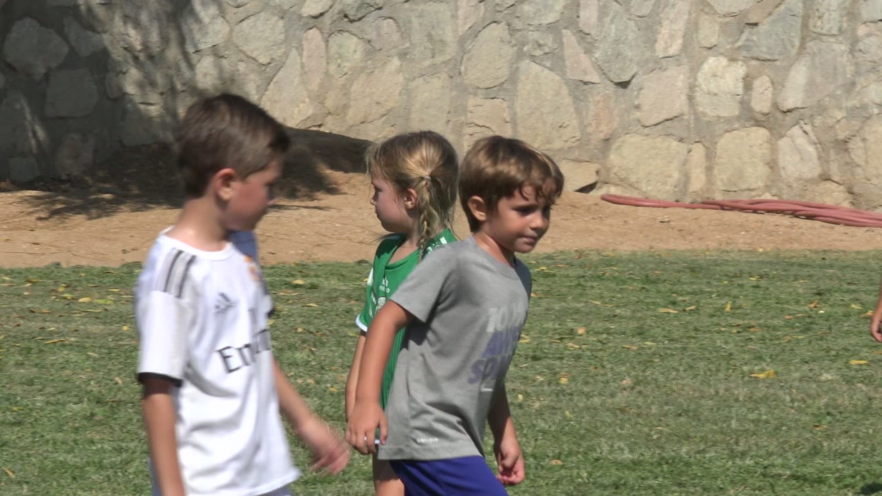 A boy in a white Real Madrid number 15 jersey walks across the field in San Jose del Cabo, Mexico, near children in green and gray shirts.