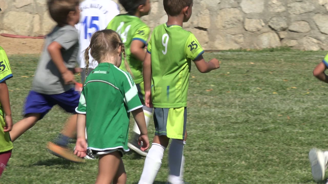 One second in, the San Jose del Cabo field is filled with children running in green and white uniforms as the foreground girl remains near the action.