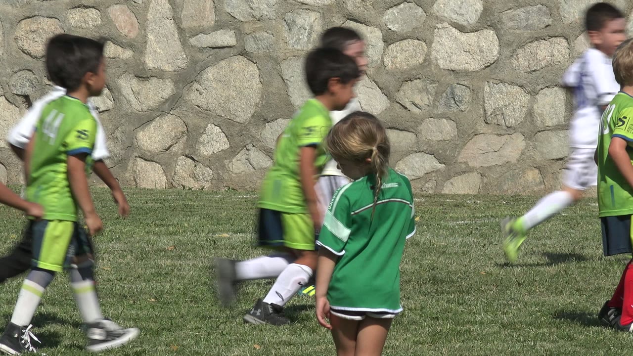 Children in green and white uniforms cross the grass in San Jose Del Cabo, Mexico, while a child in a green shirt stands nearer the camera with their back turned.