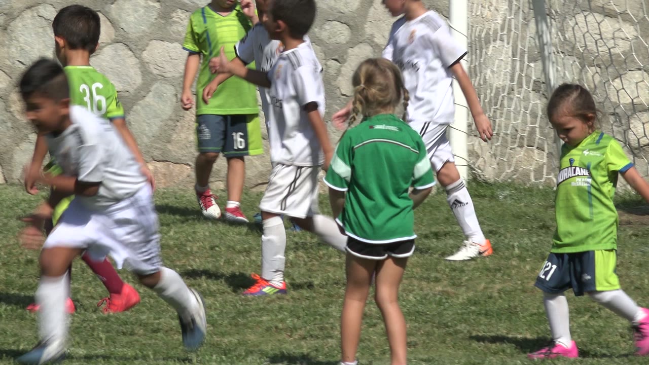 A child in a white soccer uniform runs across the foreground while children in green jerseys stand and walk near the net in San Jose del Cabo, Mexico.