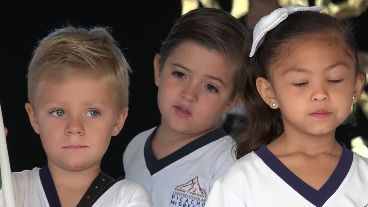 Girl with a white hair bow stands in front of other children.
