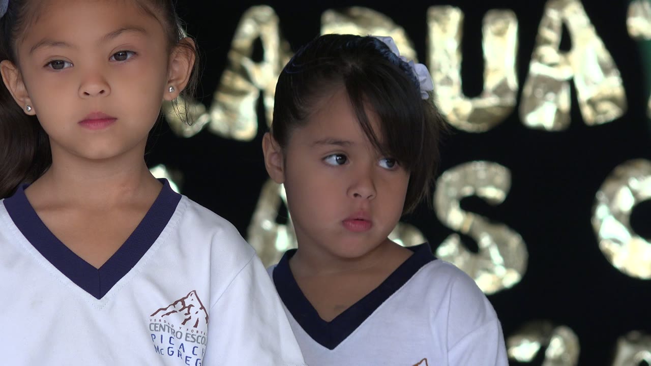 The taller girl faces forward while the younger girl looks sideways in front of shiny graduation balloon letters in San Jose del Cabo, Mexico.