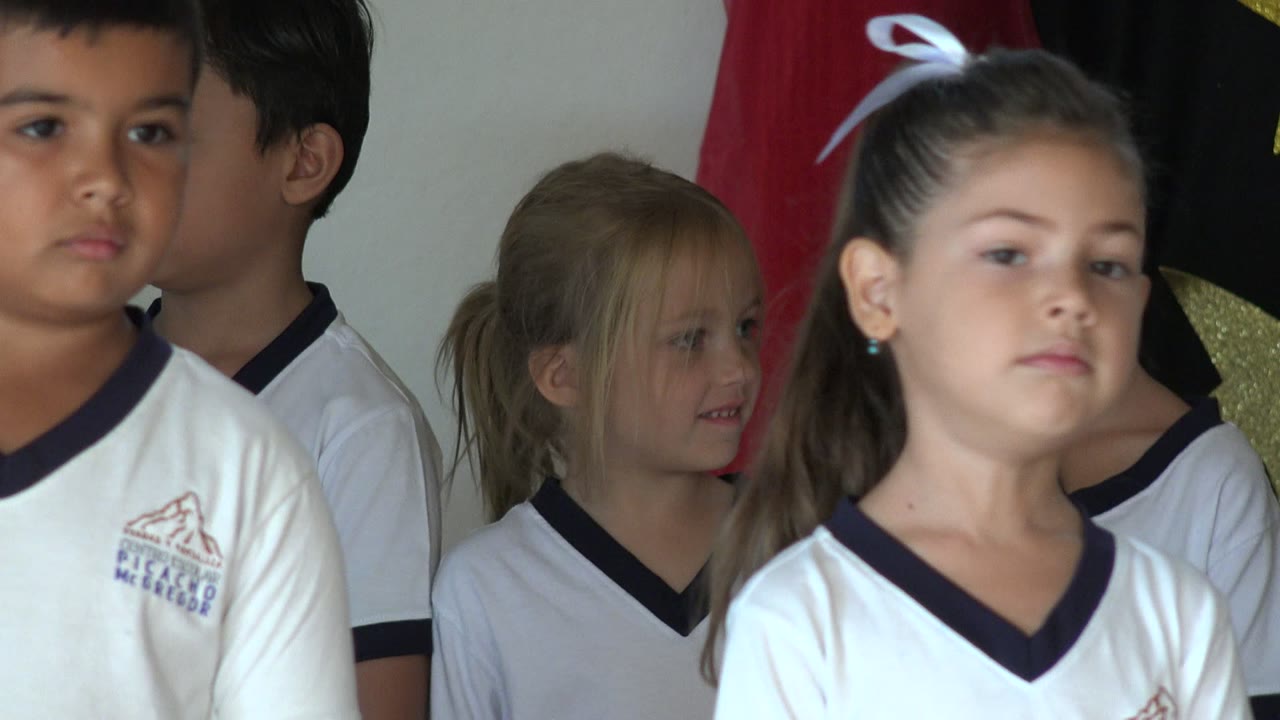 Close group of children in white shirts standing indoors.