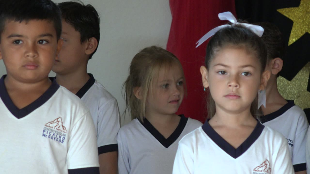 A girl with a white hair bow stands near the center among other children in white shirts inside a decorated room in San Jose del Cabo, Mexico.