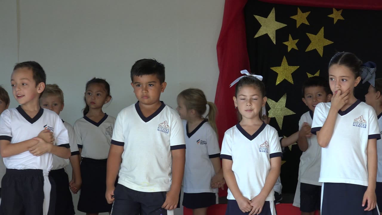 Children in white uniforms standing in front of a star backdrop.