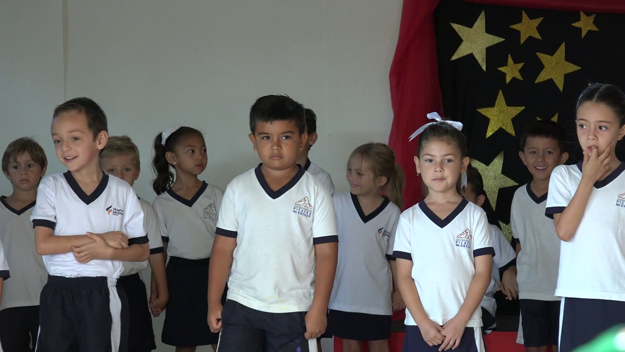 A group of children in San Jose del Cabo wait in uniform, with a girl near the right touching her mouth and the star-patterned backdrop centered behind them.