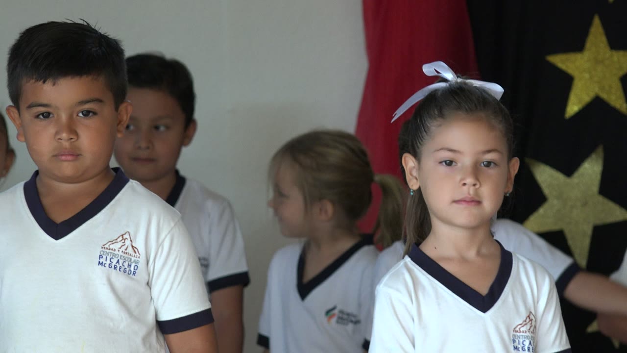 Boy in a white shirt stands near other children indoors.