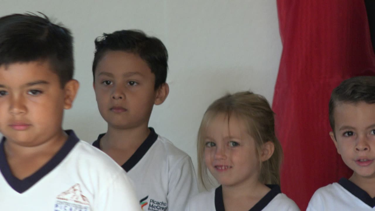 Children in white school uniforms standing in front of red curtains.