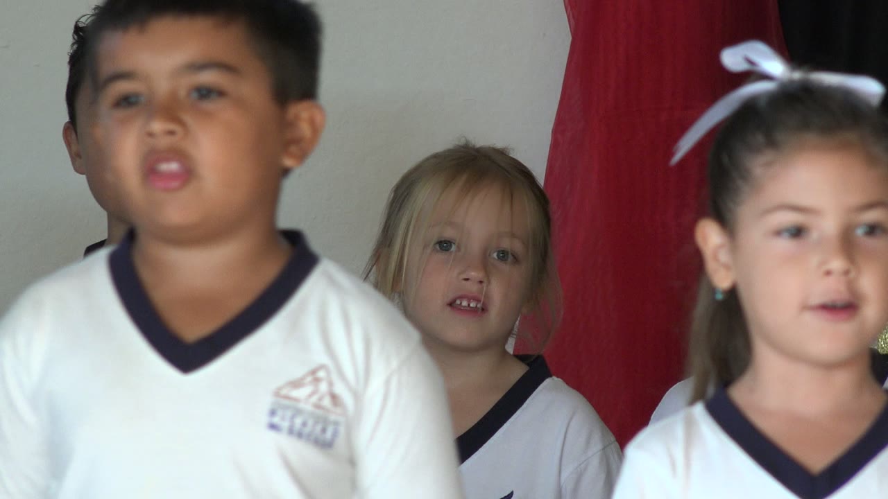 Children in white shirts stand indoors near a red object.