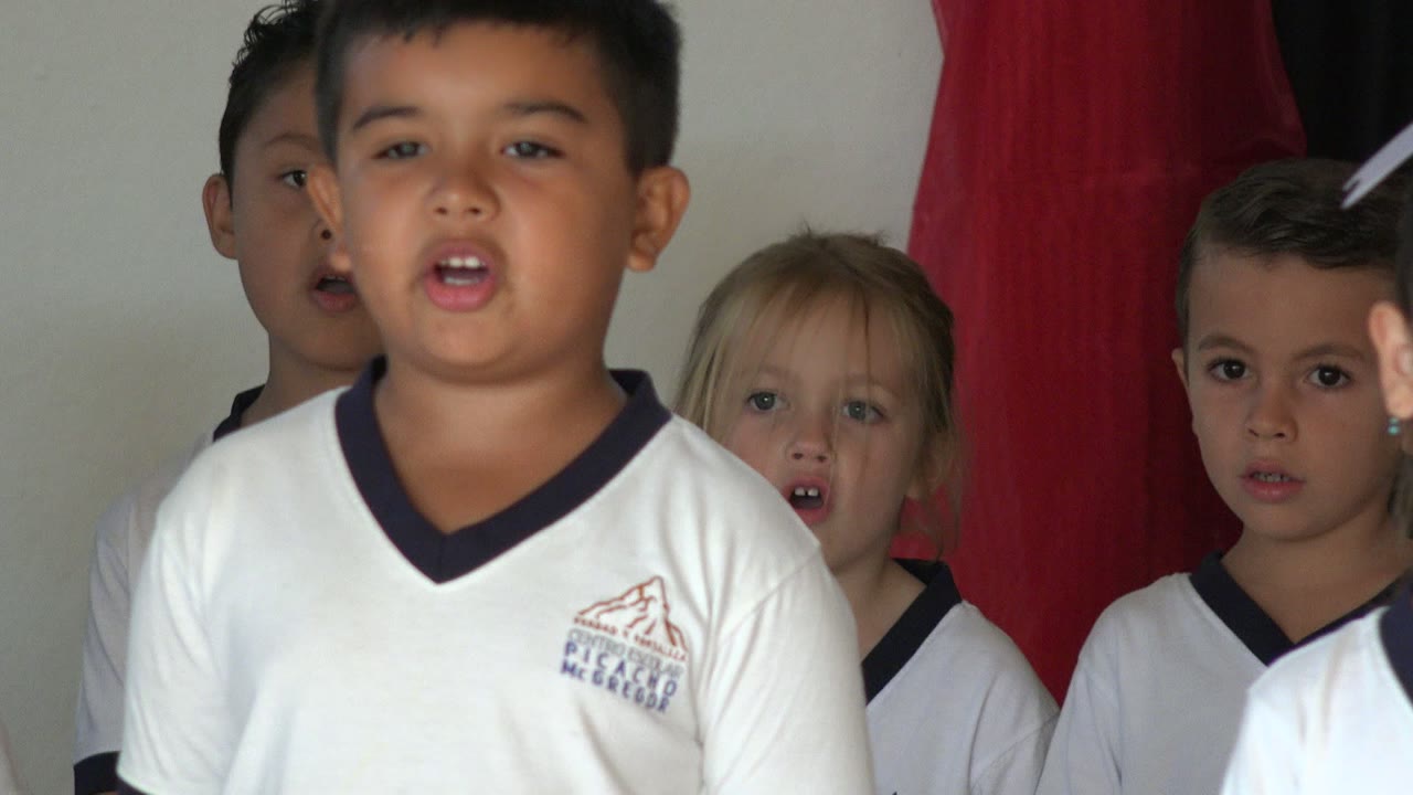 A boy in a white soccer uniform stands near the front of the group in San Jose del Cabo, Mexico, with other children partially visible behind him.