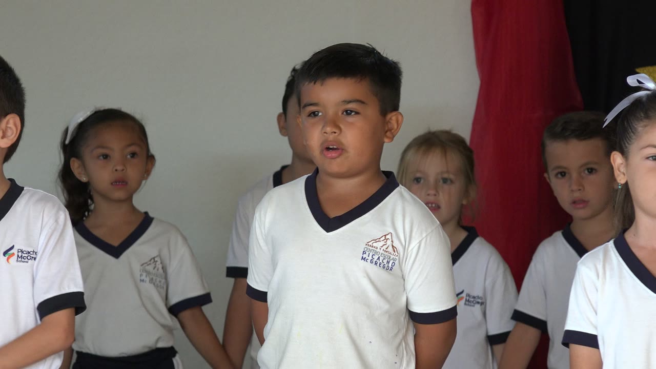 Children in white school shirts singing indoors.