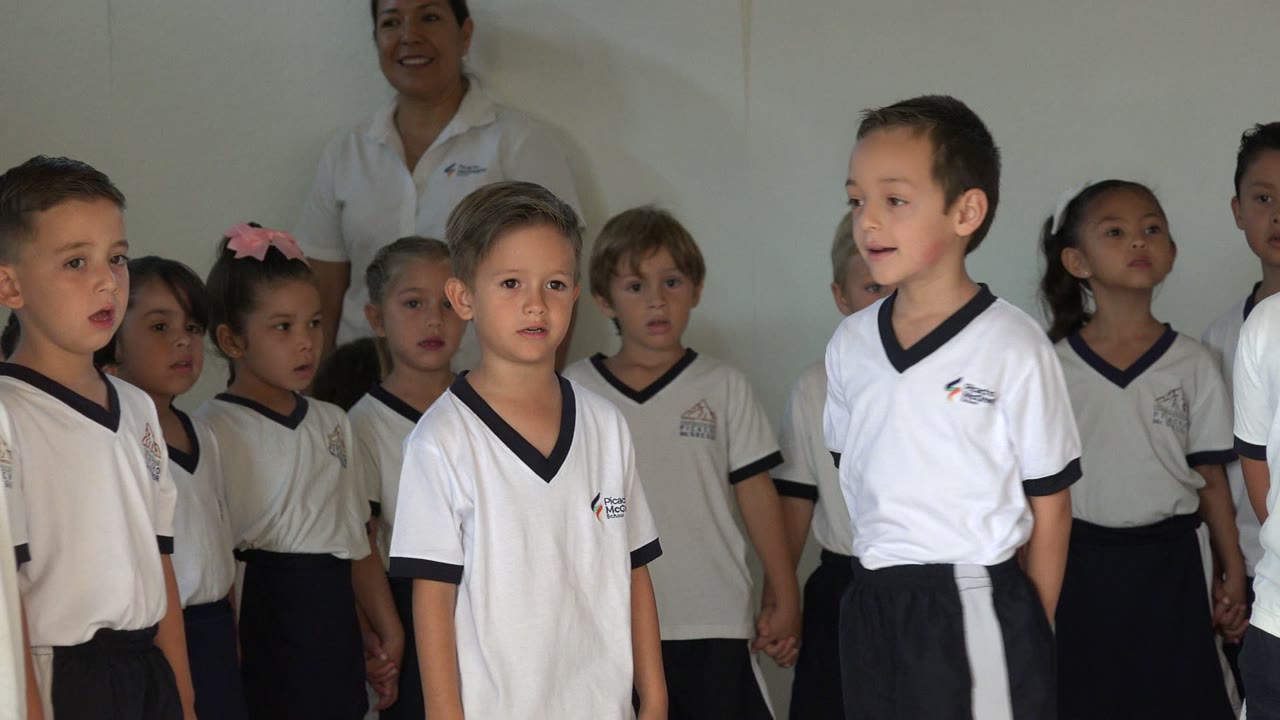 A boy in a white shirt stands near the front of the singing group in San Jose del Cabo, Mexico, with children and adults filling the background.