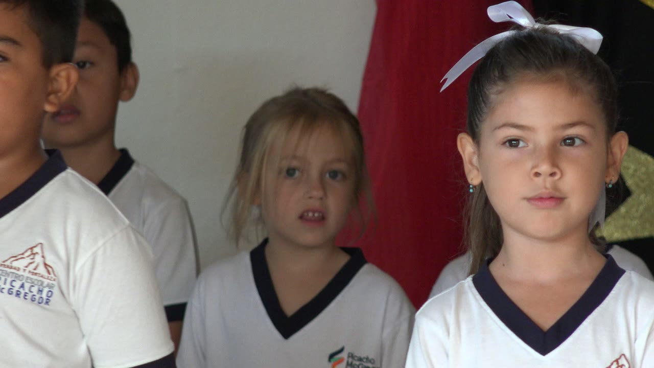 At 0:01, a girl with a white hair bow stands near the front while other uniformed children remain behind her on the San Jose del Cabo stage.