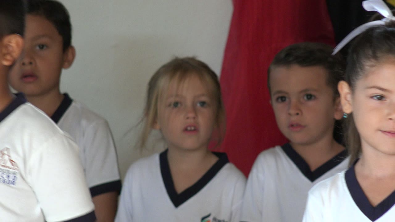 Children in school uniforms singing with a red curtain backdrop.