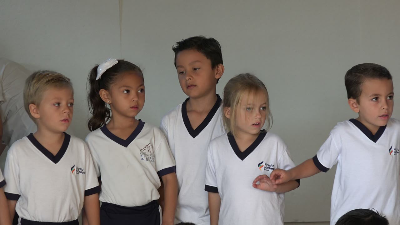 Preschool children in white uniforms standing in a classroom line.