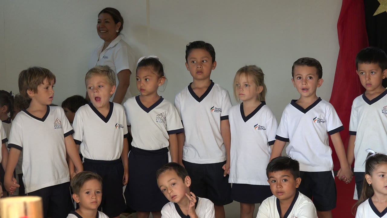 In San Jose del Cabo, Mexico, the line of uniformed children shifts slightly, with several children looking sideways and an adult woman visible behind them near the wall.