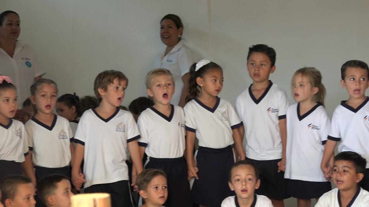 Children sing in a row with a red curtain at the side.