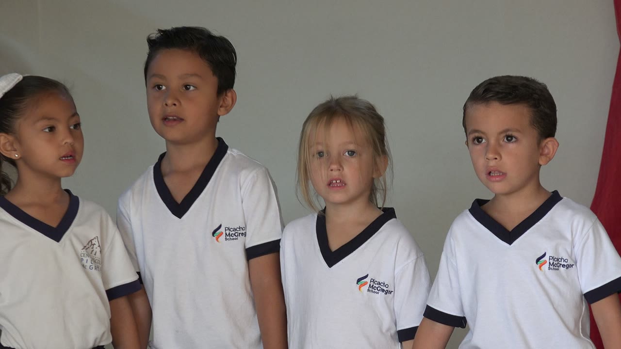 Four children in white school uniforms standing in a line