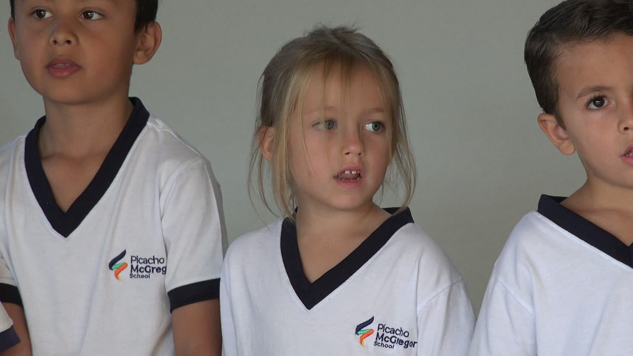 A blond girl in a white uniform shirt looks off to the side in San Jose del Cabo, Mexico, while another child is partly visible at the right edge against a plain wall.