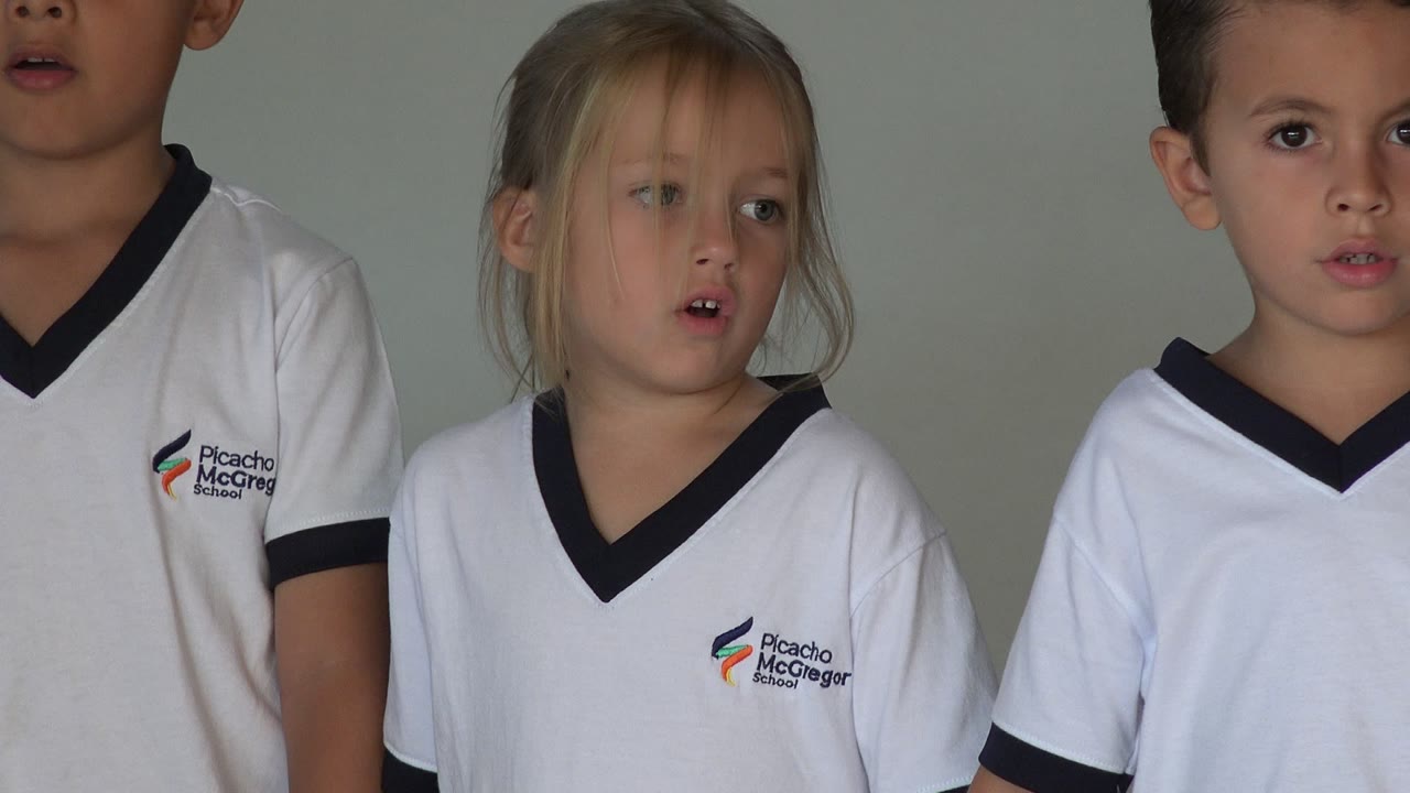 Cropped view of children in white school shirts standing indoors.