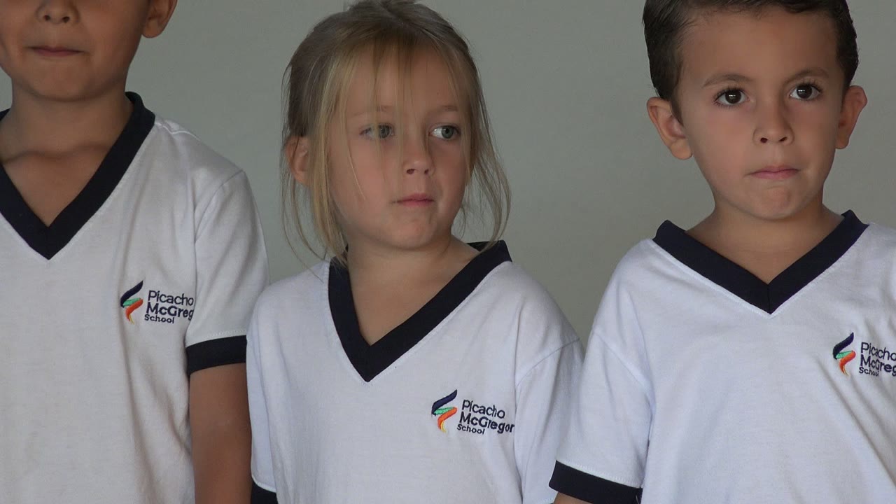 Two young boys in white school shirts are framed closely in San Jose Del Cabo, with one boy in front looking toward the camera and another standing just behind him.