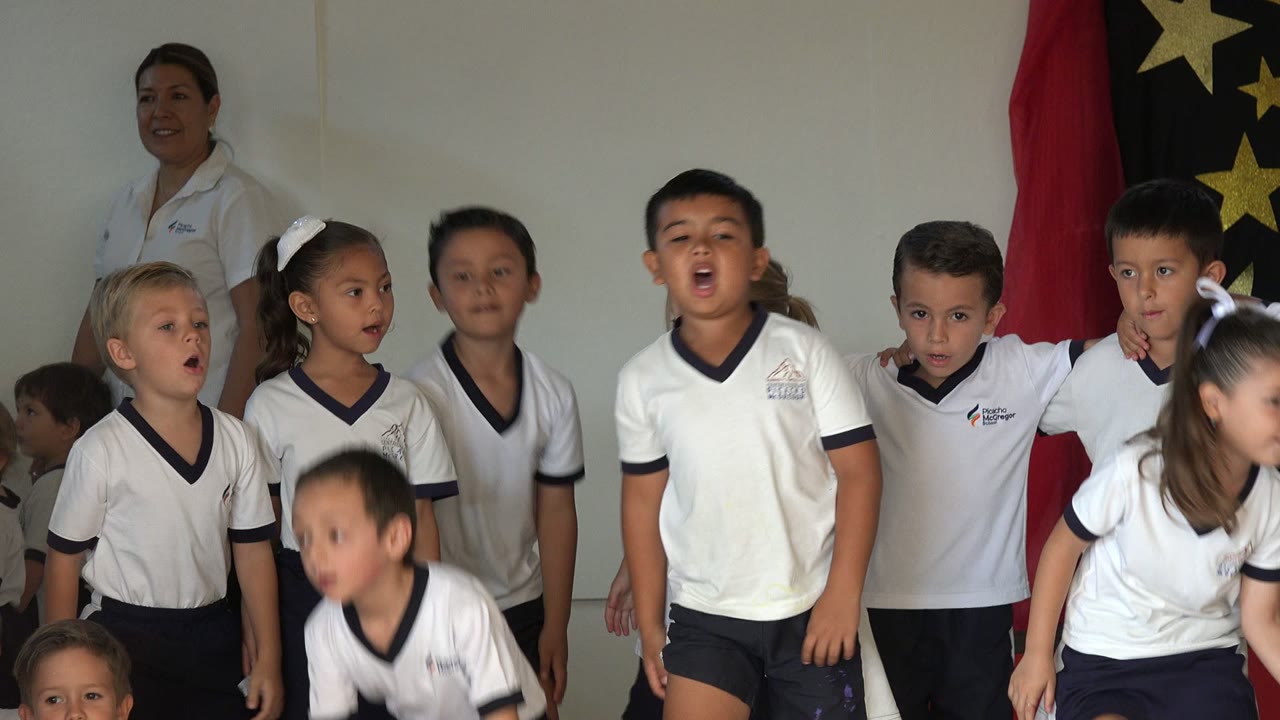 At 0:01 in San Jose del Cabo, Mexico, the children stand more centered as several look forward and a black backdrop with gold stars appears behind the group.
