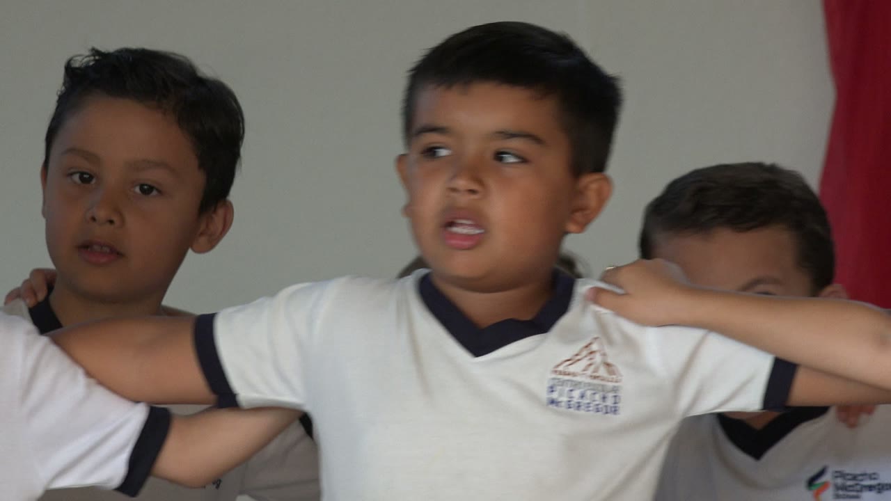 Children in white shirts stand with arms linked in a tight group.