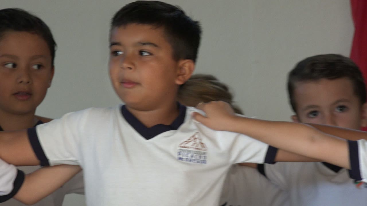 A central boy in San Jose del Cabo looks to the side with his arm extended across another child's shoulder, while classmates remain closely grouped behind him.