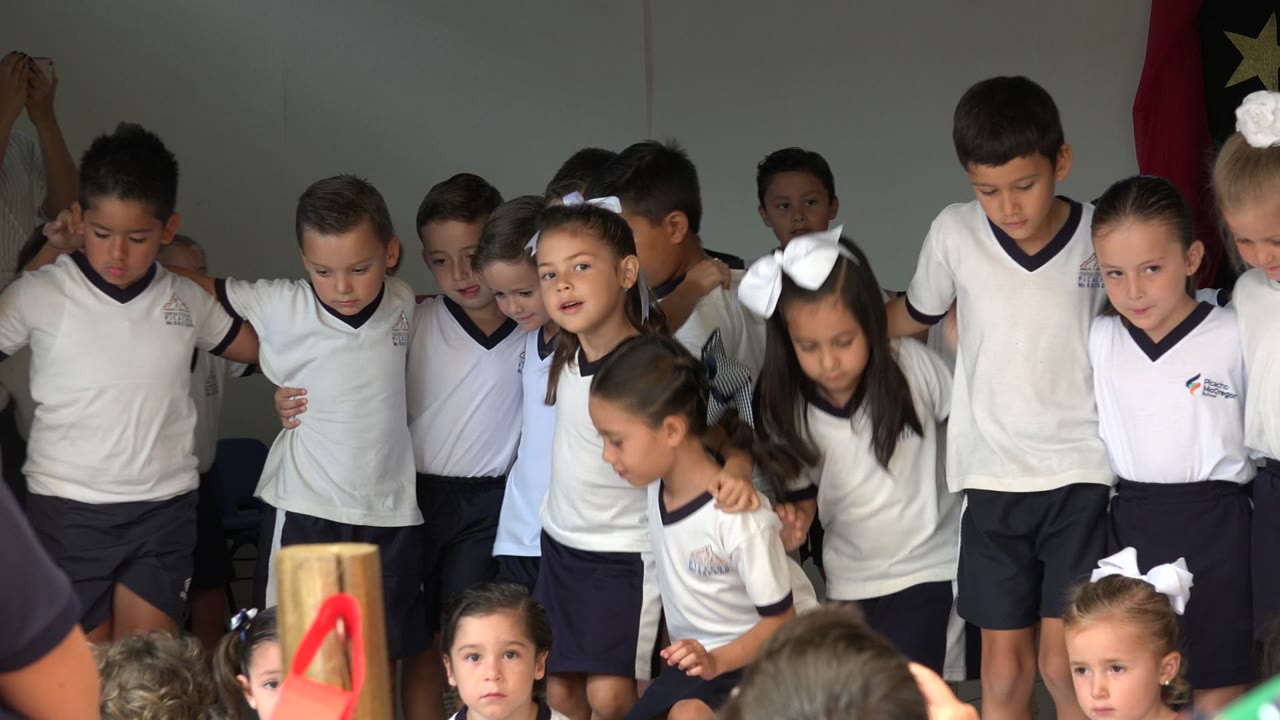 Schoolchildren in white uniforms gathered on a stage.