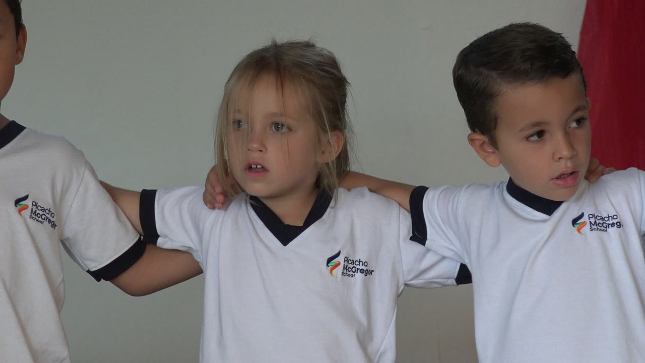 A young girl and boy in white uniforms stand shoulder to shoulder in San Jose del Cabo, Mexico, with another child partly visible behind them.
