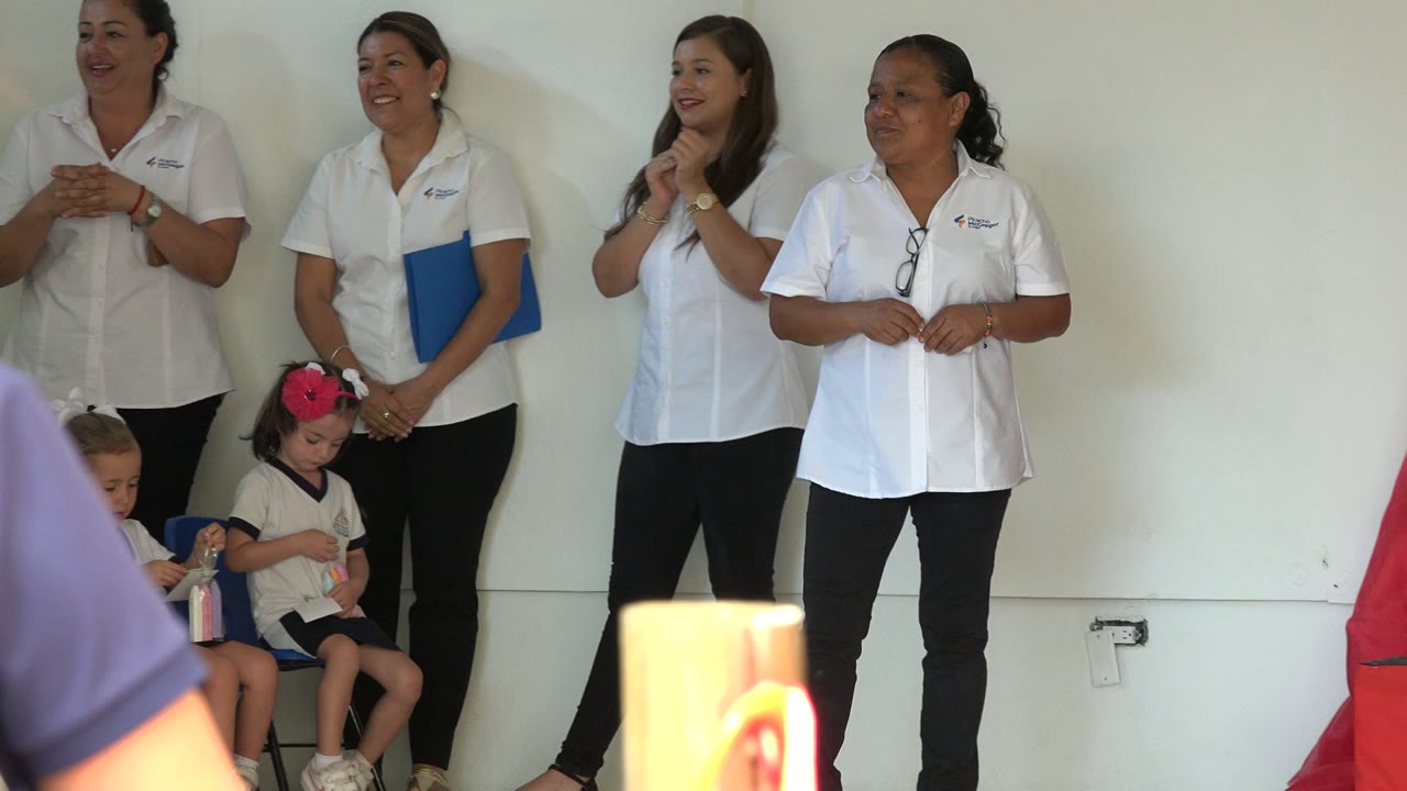 In San Jose del Cabo, Mexico, the row of women remains centered, one holds a blue folder, two seated girls are visible near their legs, and a blurred shoulder crosses the lower foreground.