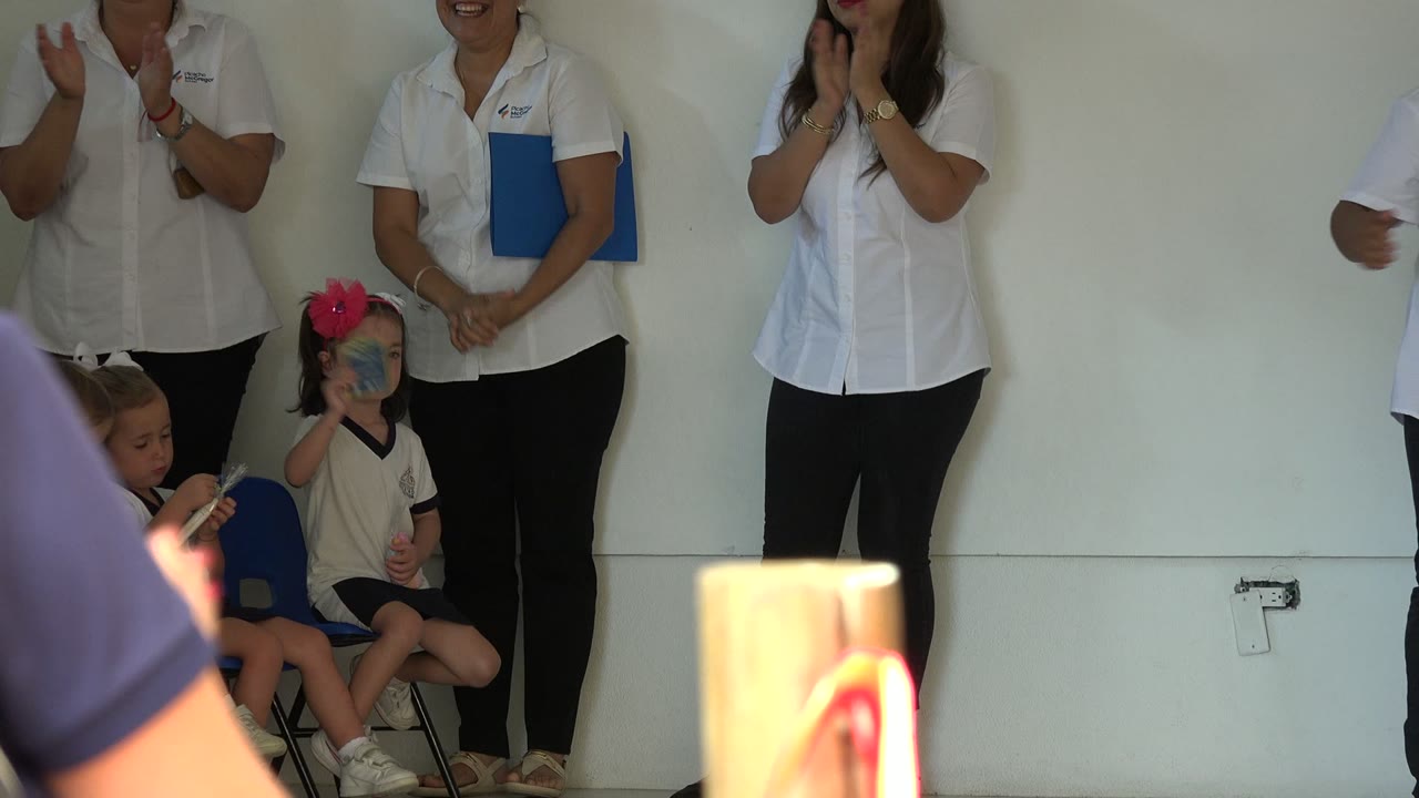 Adults stand by seated children near a small stage.