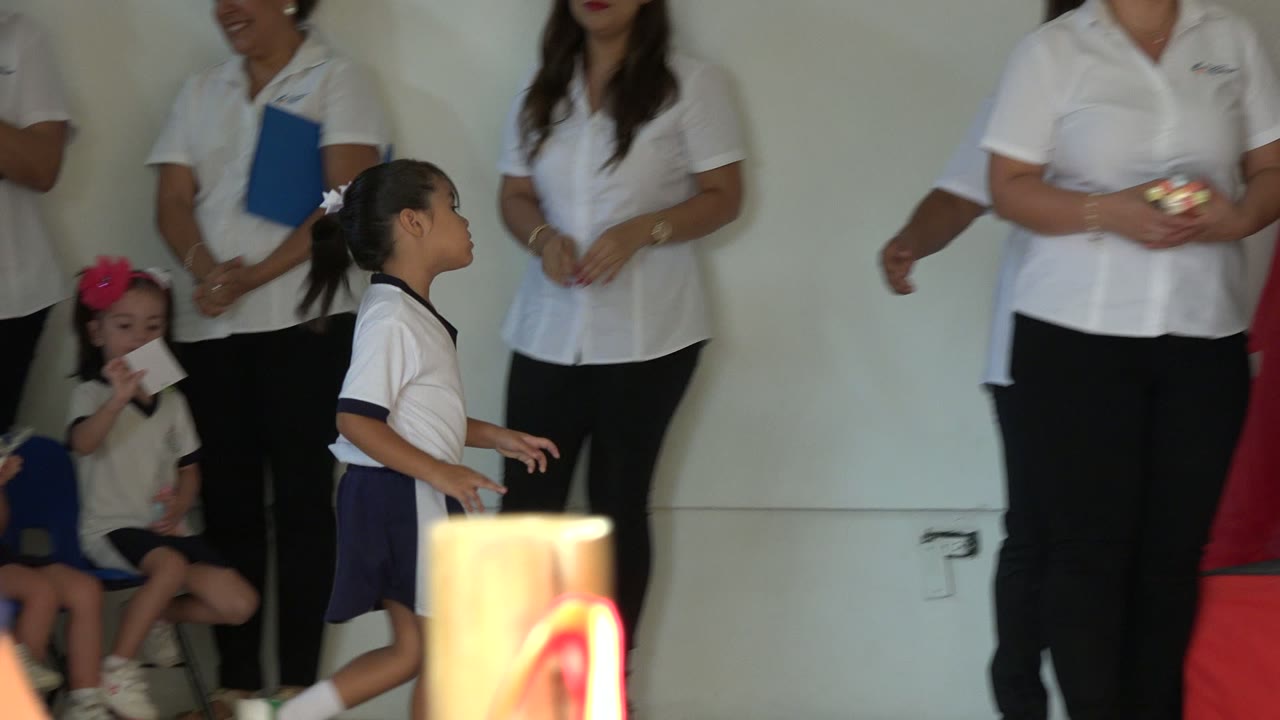 A young child in a white shirt and navy shorts walks toward the stage in San Jose del Cabo while adults and another child wait behind him.