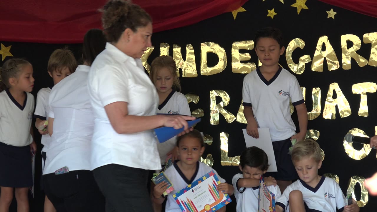 Teacher stands beside children on a decorated school stage.