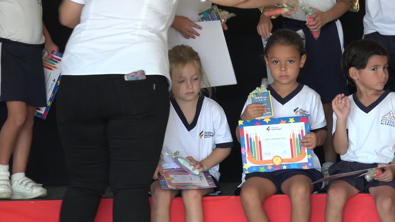 Young girls seated with certificates while adults stand behind them.