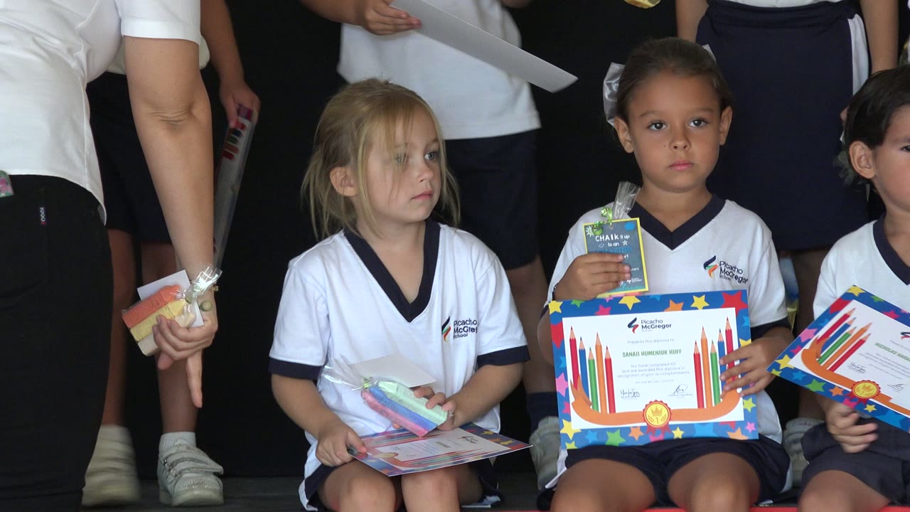 The middle girl looks aside as another girl holds up a certificate and a small wrapped item during the awards moment in San Jose del Cabo, Mexico.