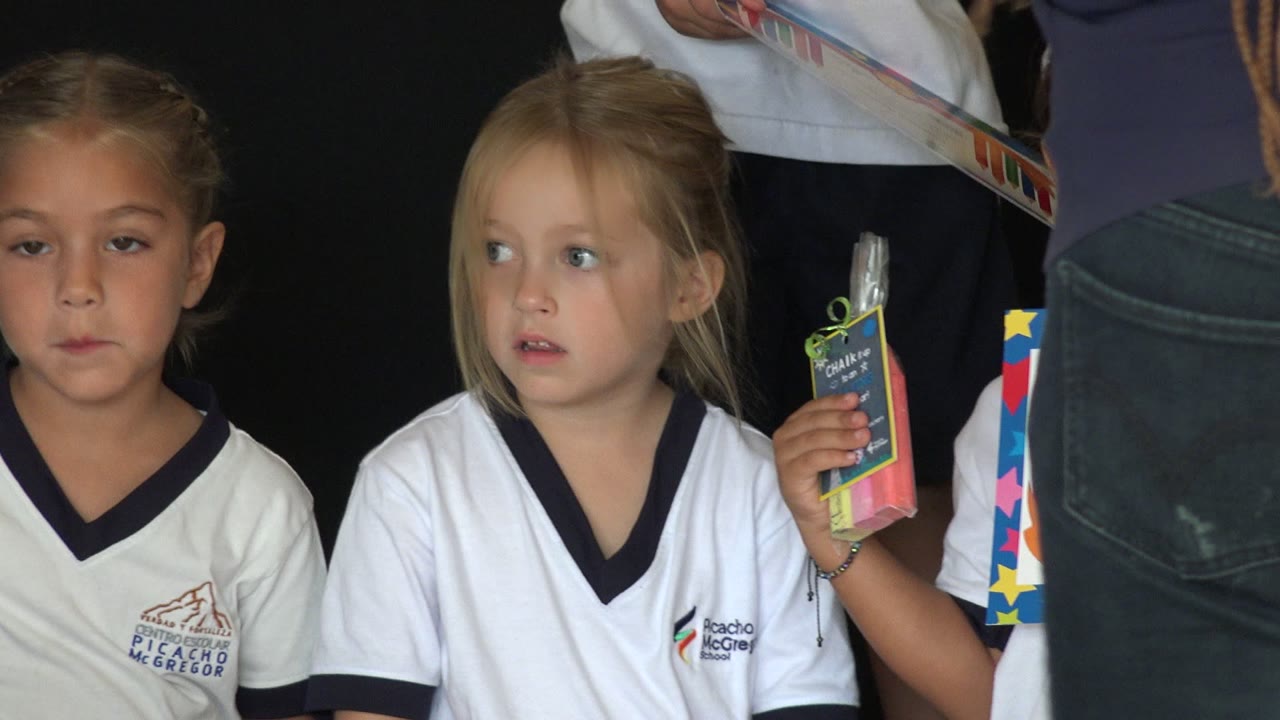 Two young girls in white school shirts against a dark background.