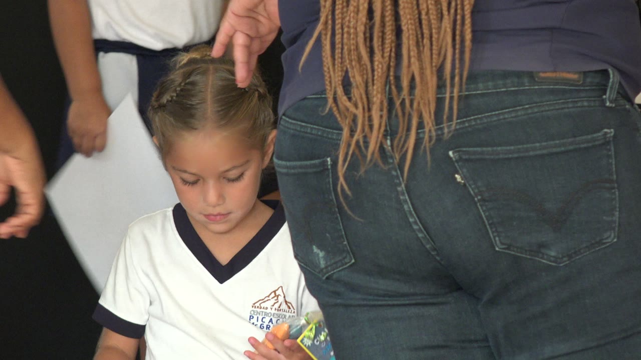 A young girl in a white school shirt looks down on a decorated stage in San Jose Del Cabo, Mexico, while adults stand close in the foreground.