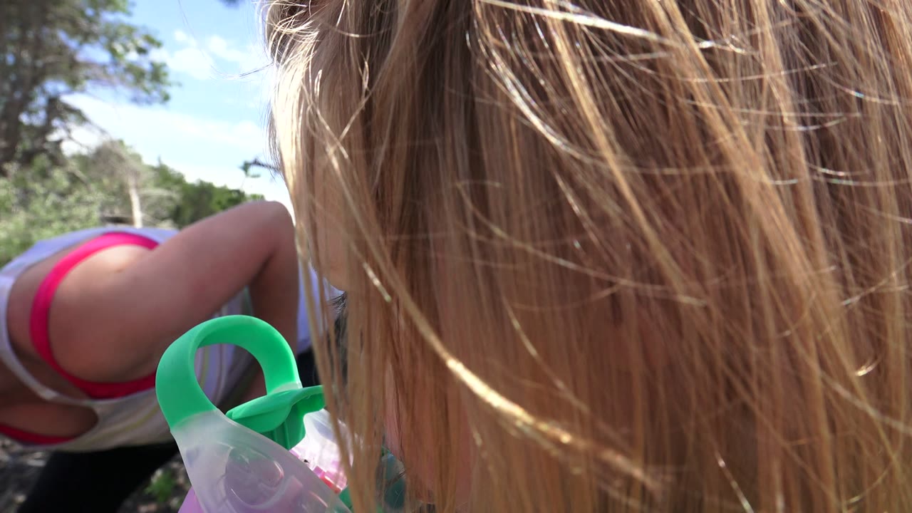 The Westminster, Colorado frame stays tight on the child's blonde hair and green-handled sippy cup while a striped-shirt adult is partially seen in the wooded background.