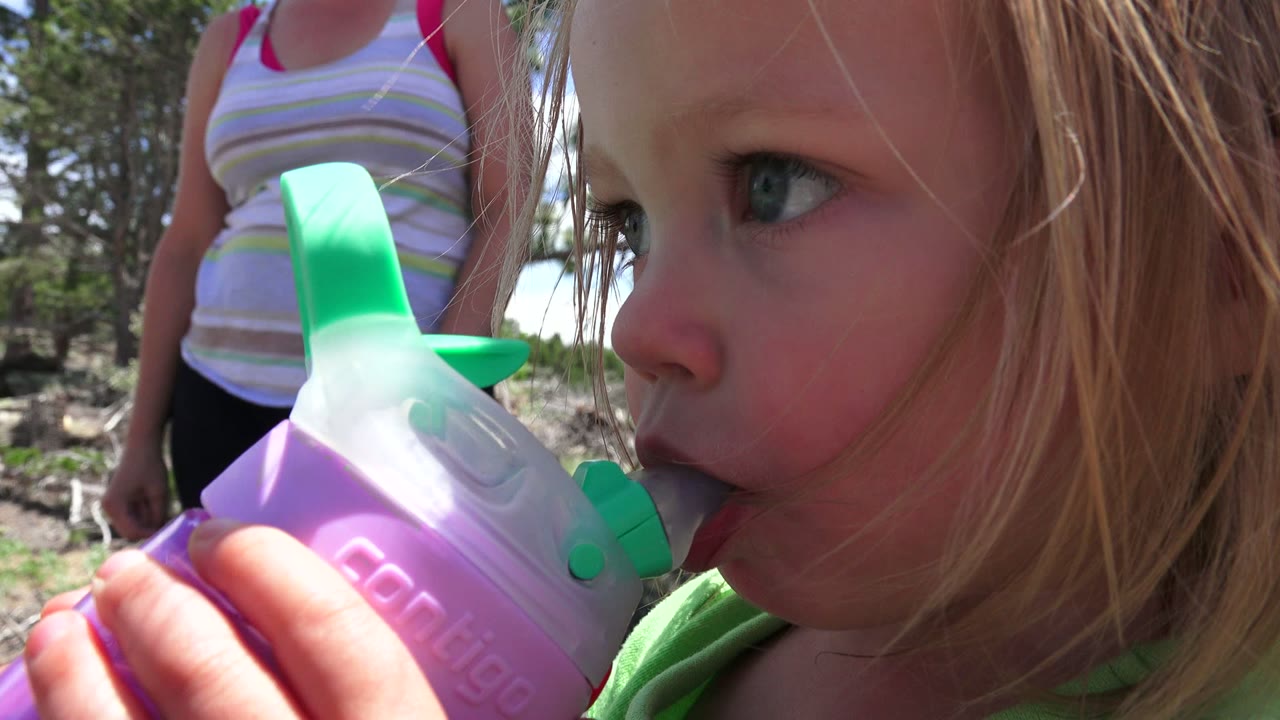 Close-up of a toddler drinking from a sippy cup in bright outdoor light.