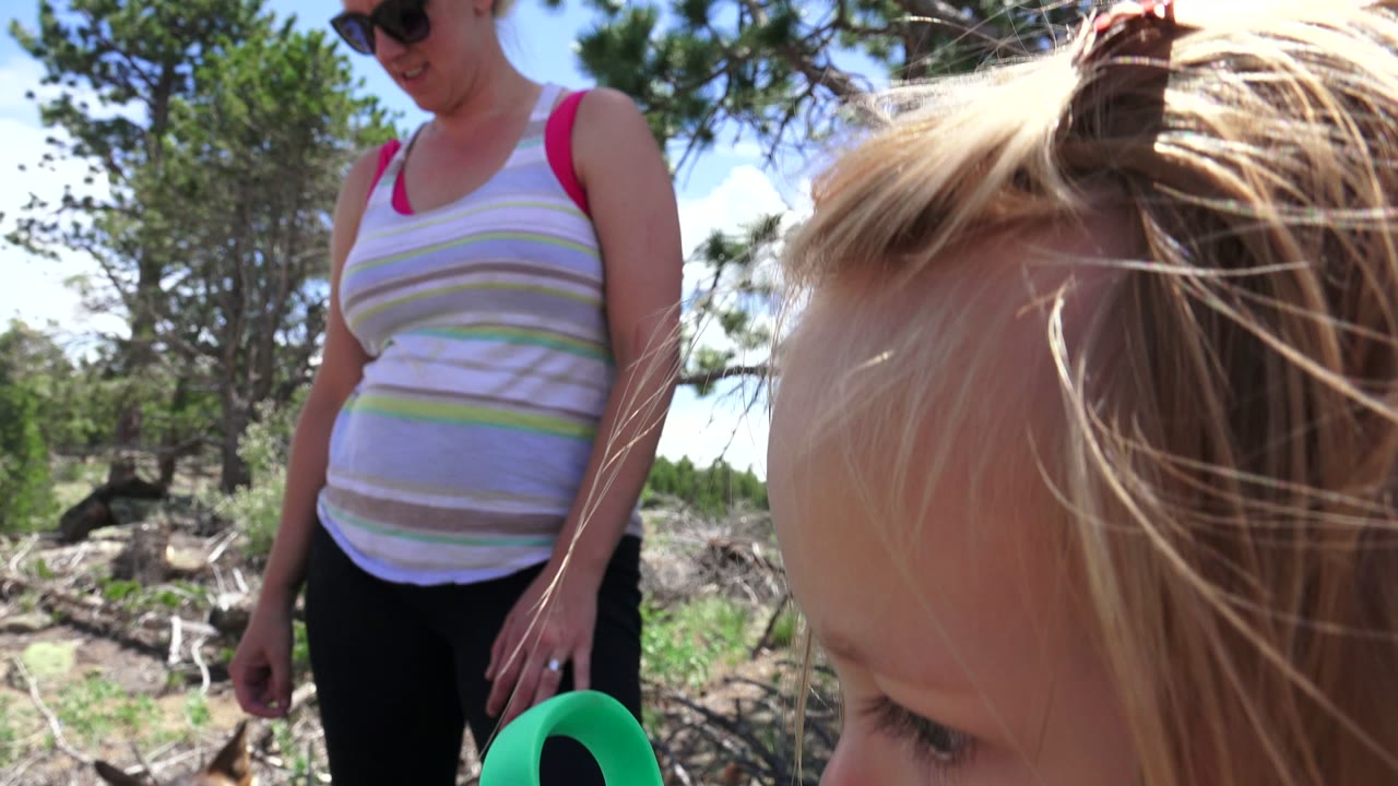 Woman standing in a forest beside a blond child close to camera.