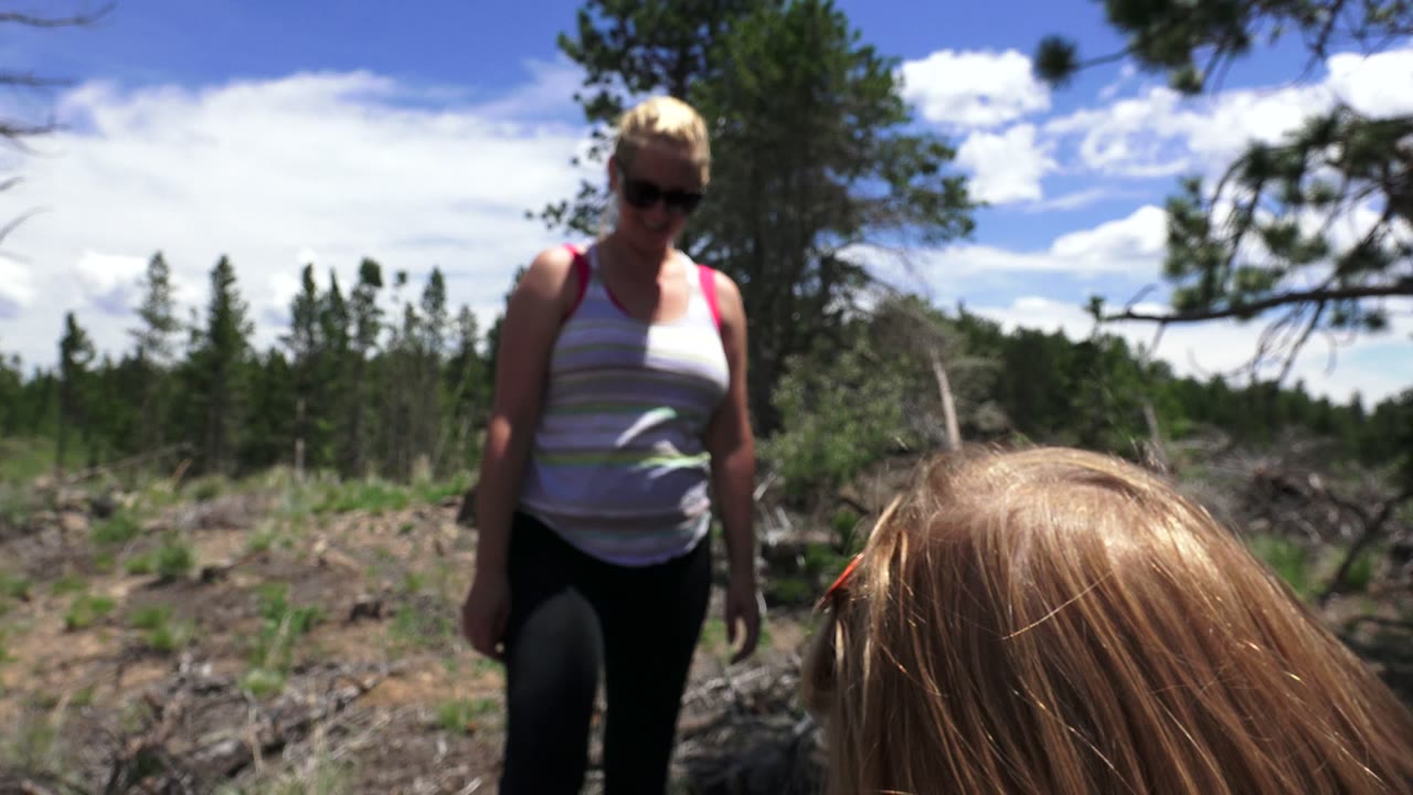 Blonde woman in sunglasses standing behind a blonde child outdoors.