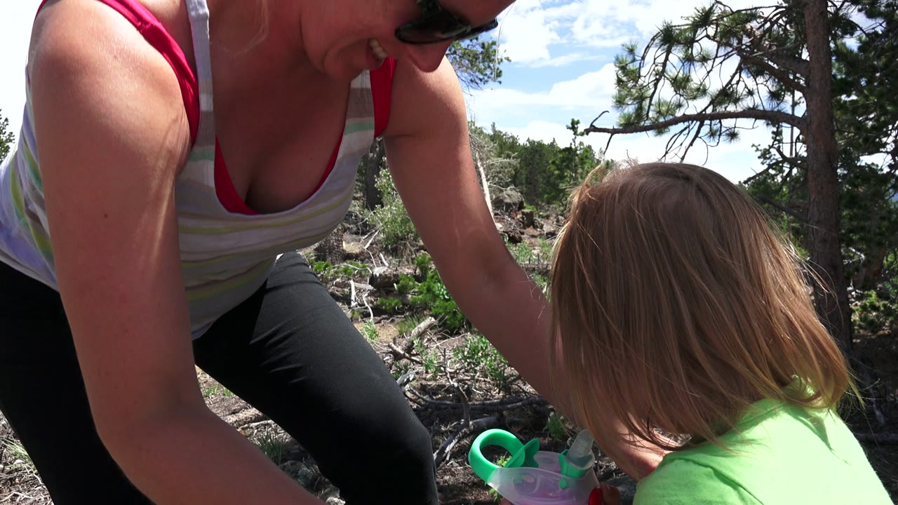 In Westminster, Colorado, an adult woman leans down toward a young girl whose head is turned away, with a cup partly visible near the lower frame edge.