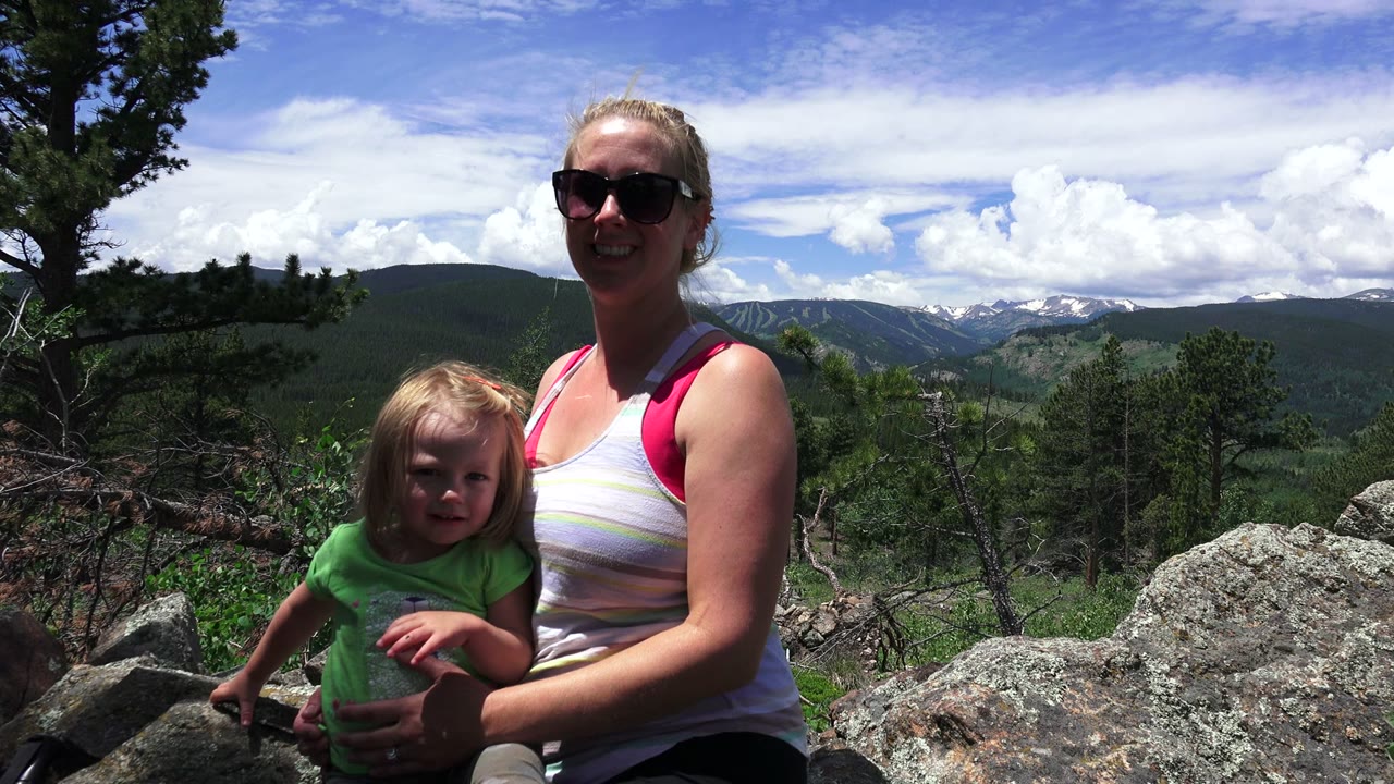 In Westminster, Colorado, the child faces toward the camera while the woman smiles beside large foreground rocks and forested hills.