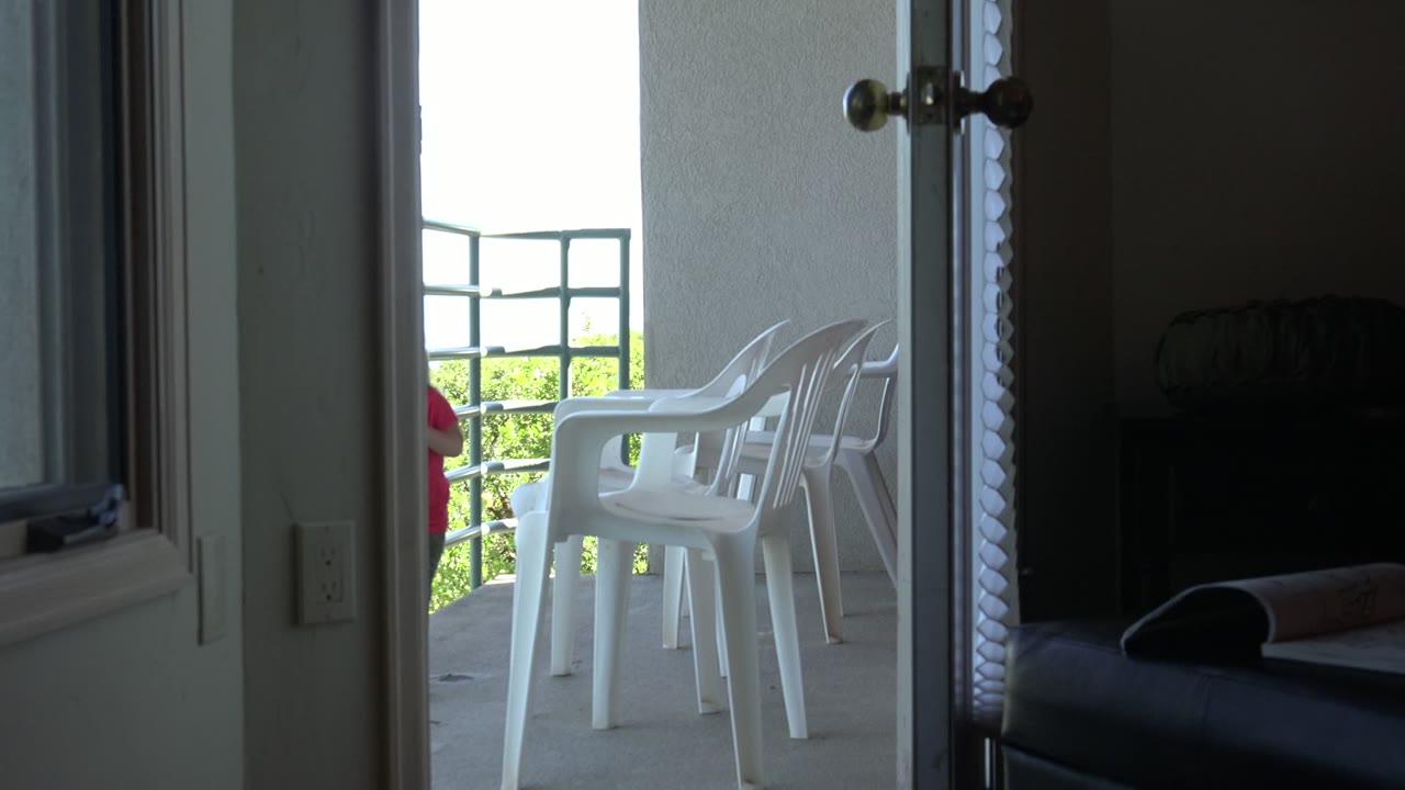 Open doorway looking onto white veranda chairs with no visible people.