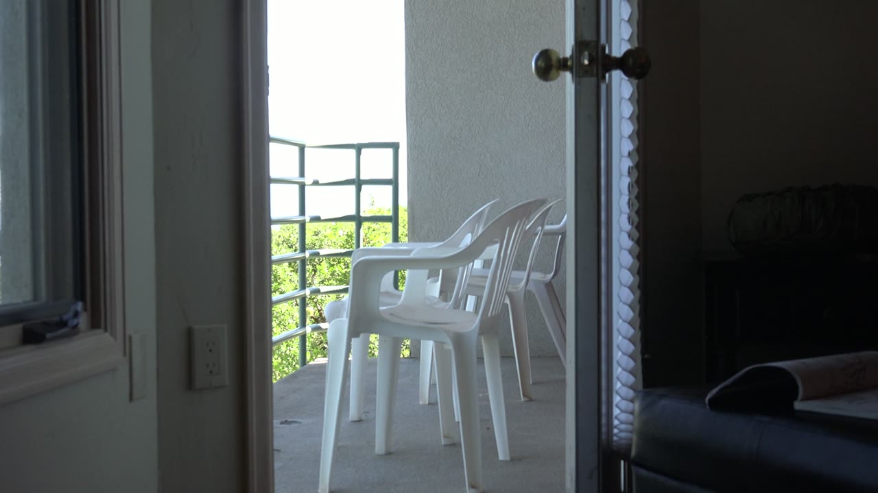 Bright veranda chairs and green railing are framed by an open doorway in Mesa, Colorado, while the right side remains a dark interior space with no visible people.