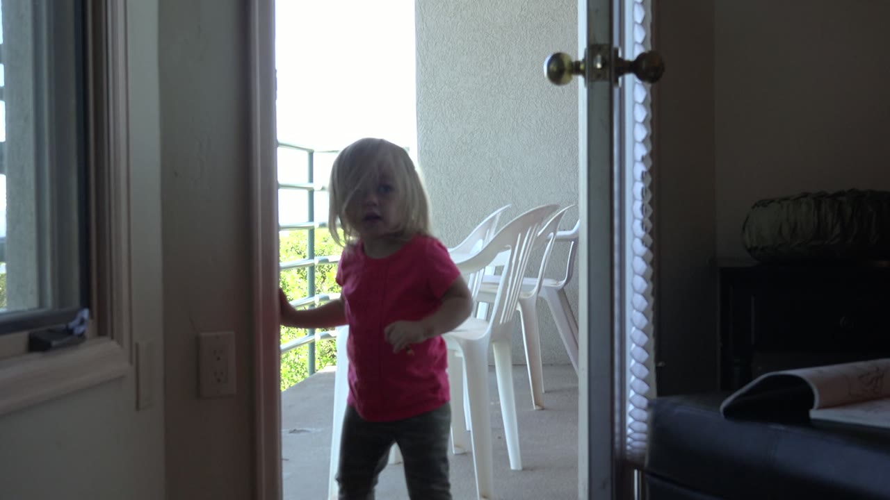 Young girl in a red shirt stepping near an open white door.