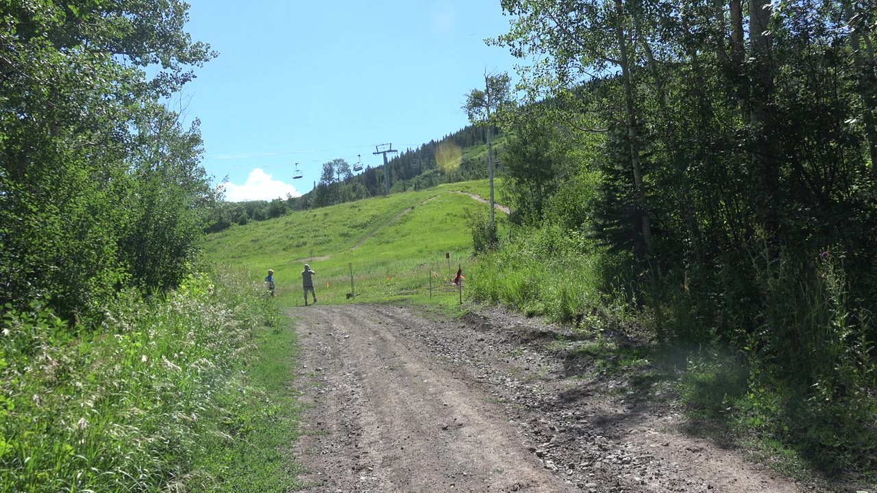 Rocky dirt road through dense greenery toward a hill with lift towers.