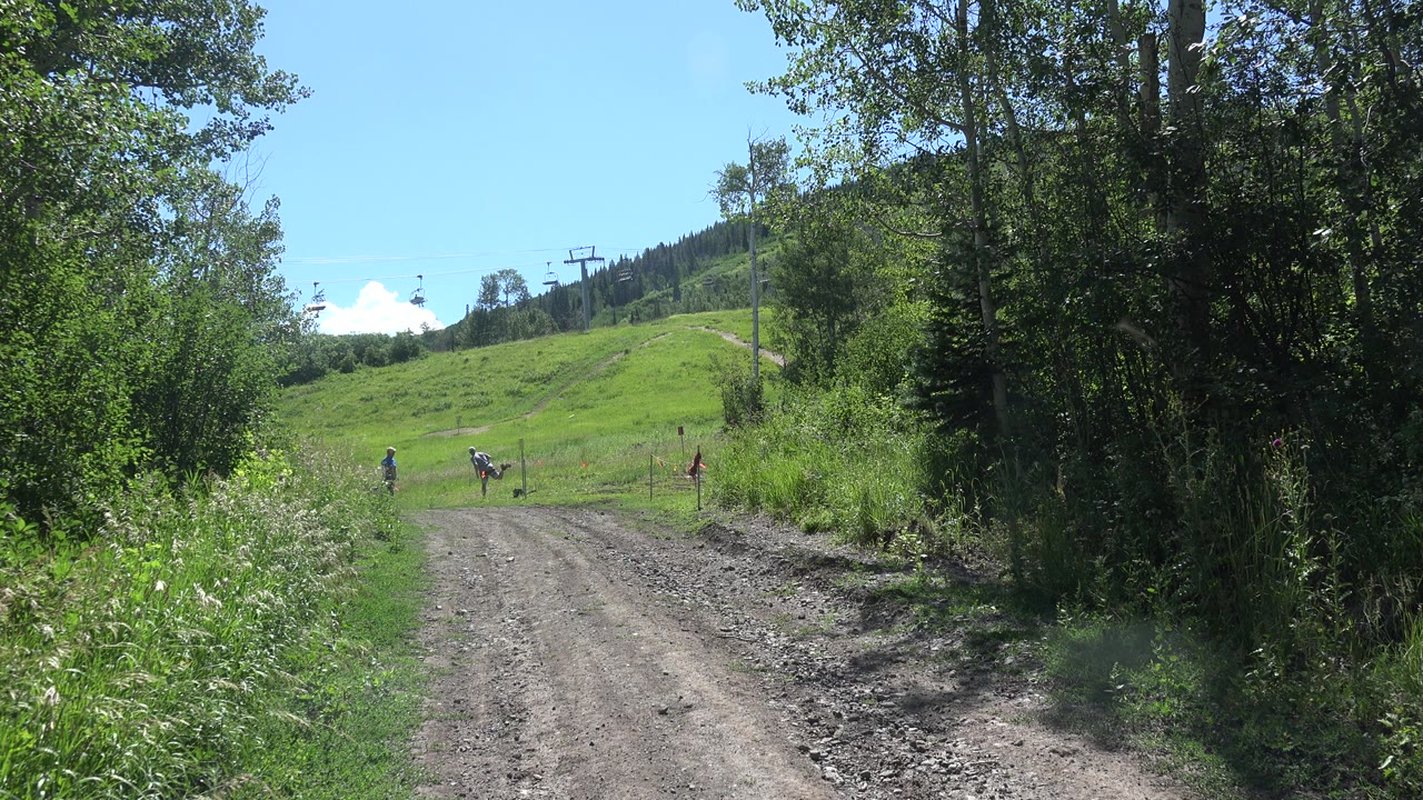 Dirt road leading toward a grassy hillside with distant people.
